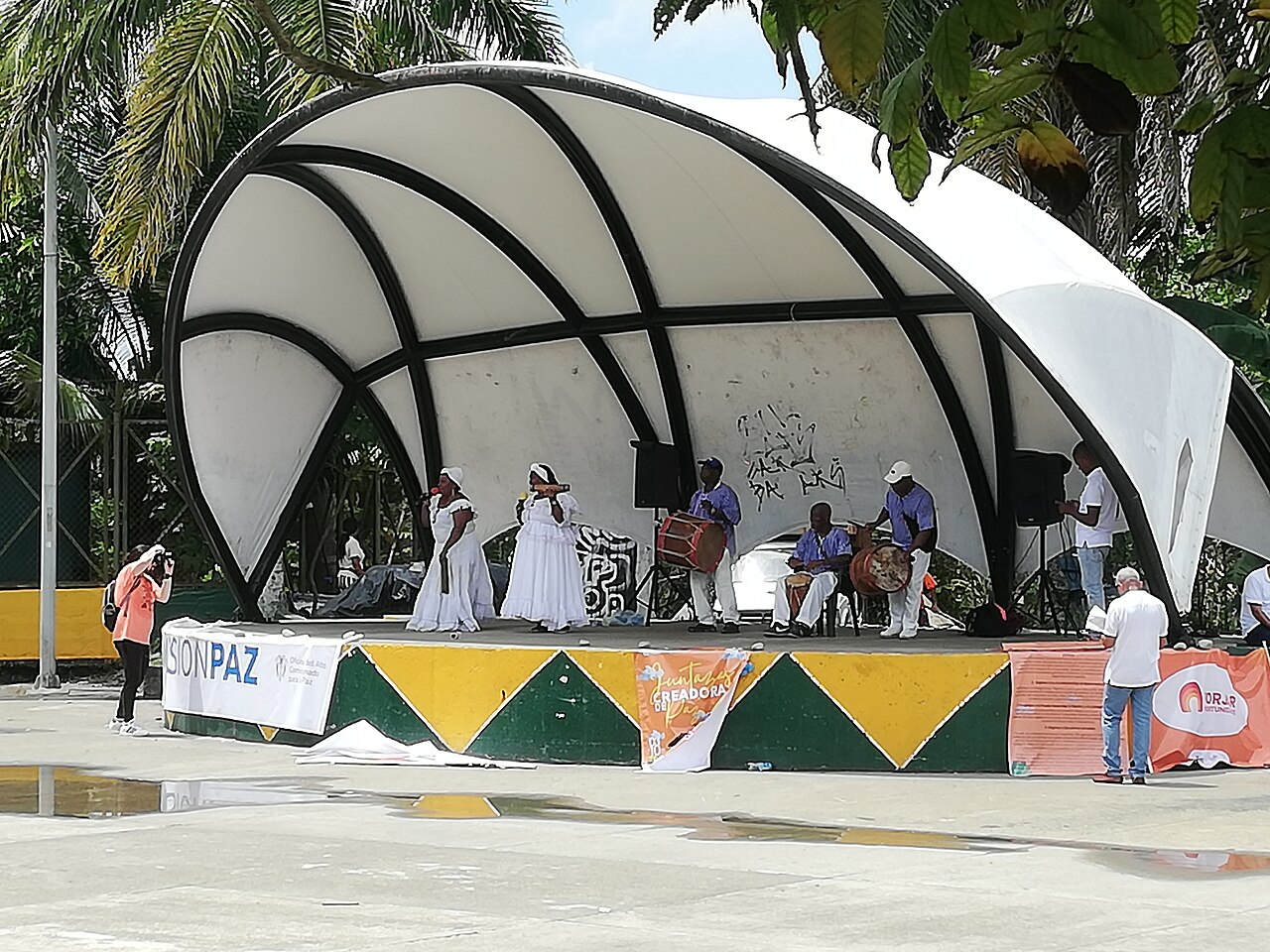 Dos mujeres cantan con percusionistas en un escenario al aire libre con cubierta acústica.