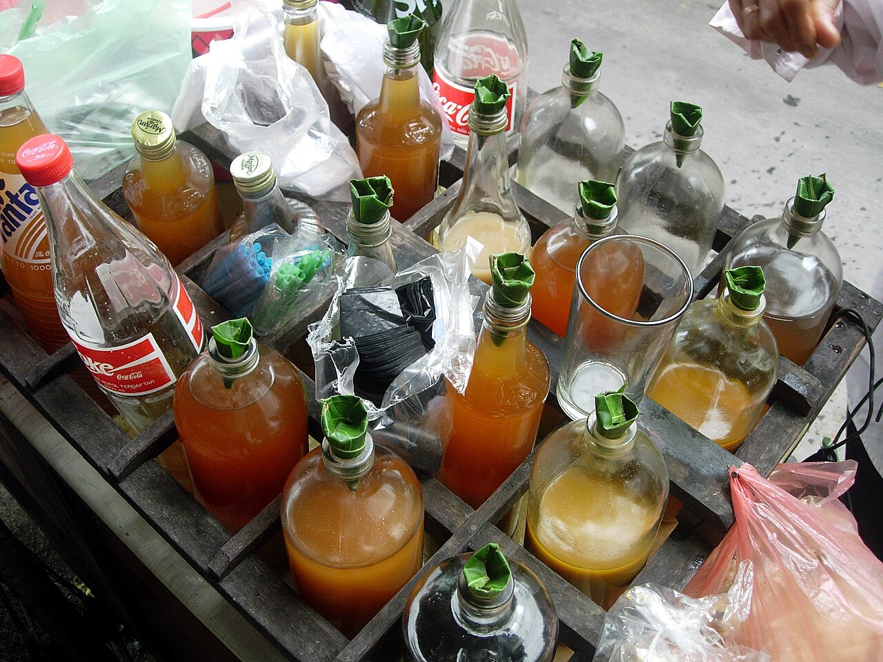 Preparados de jamu de distintos colores en botellas de vidrio colocadas en un soporte de transporte.