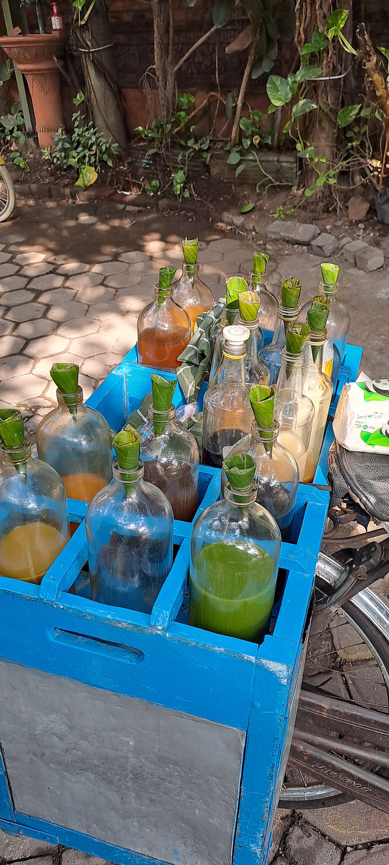 Glass bottles with leaf stoppers in a blue carrier beside a motorbike.