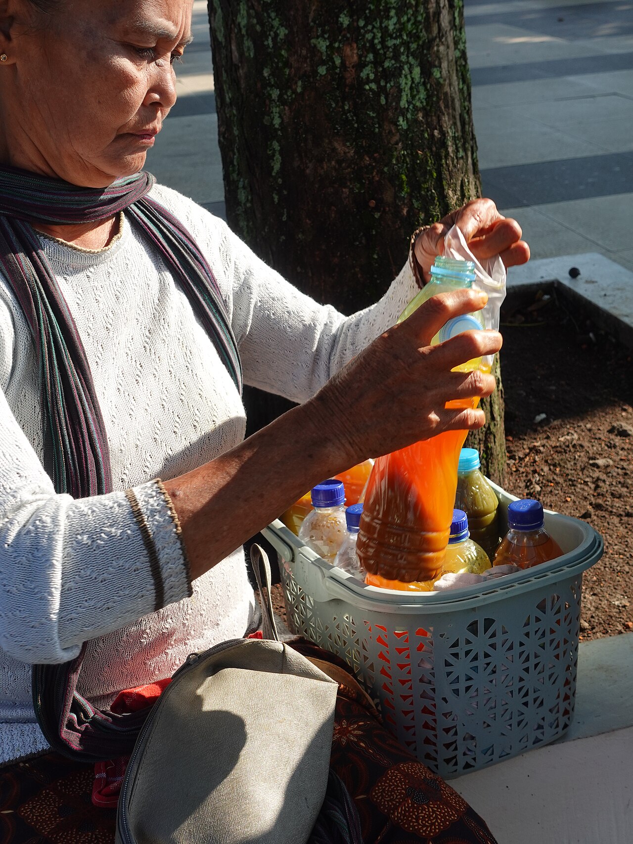 Una mujer vierte una bebida naranja de una botella de plástico a una bolsa.