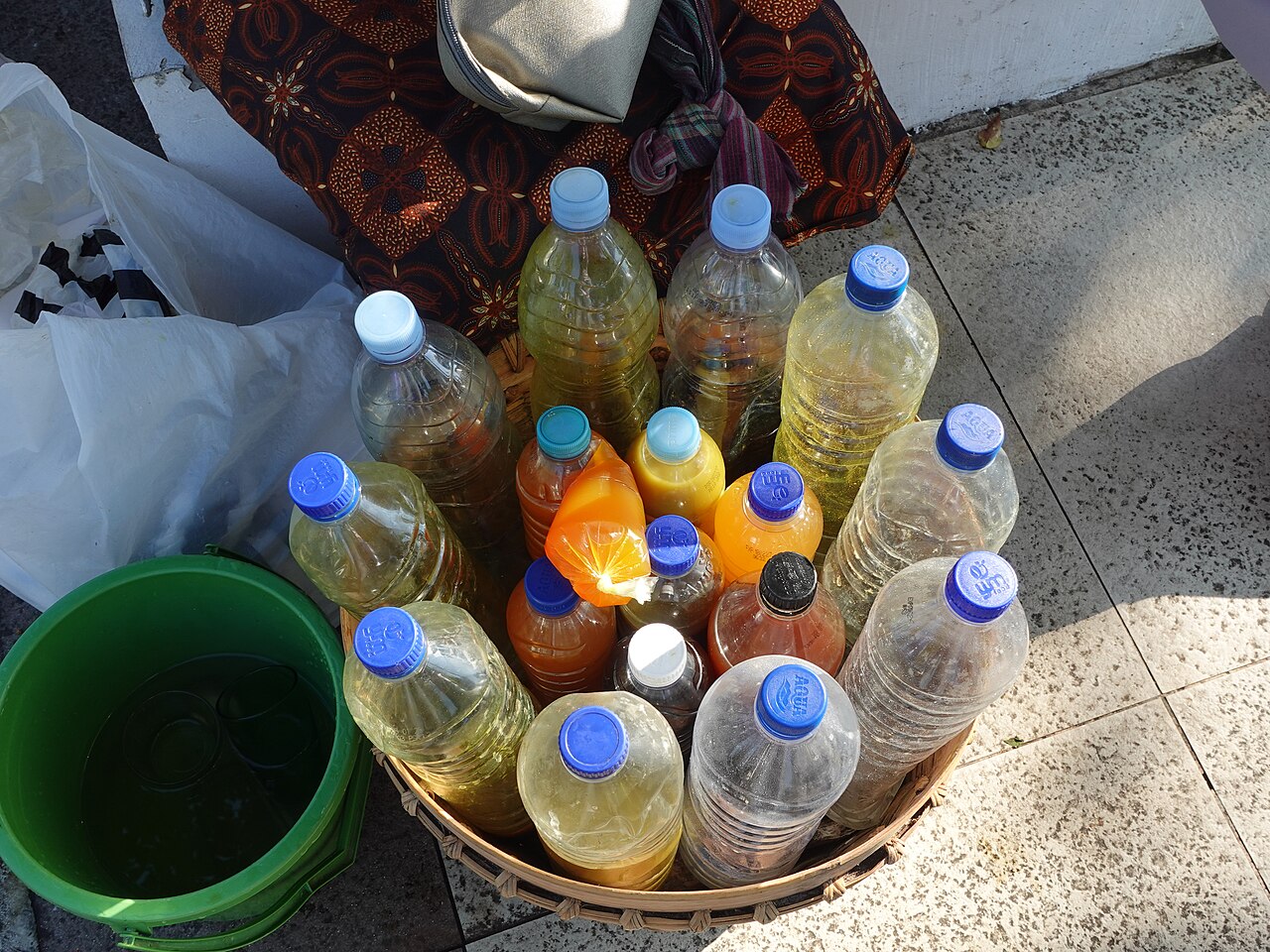 Bebidas amarillas y naranjas en botellas de plástico dentro de una cesta tejida, junto a vasos.