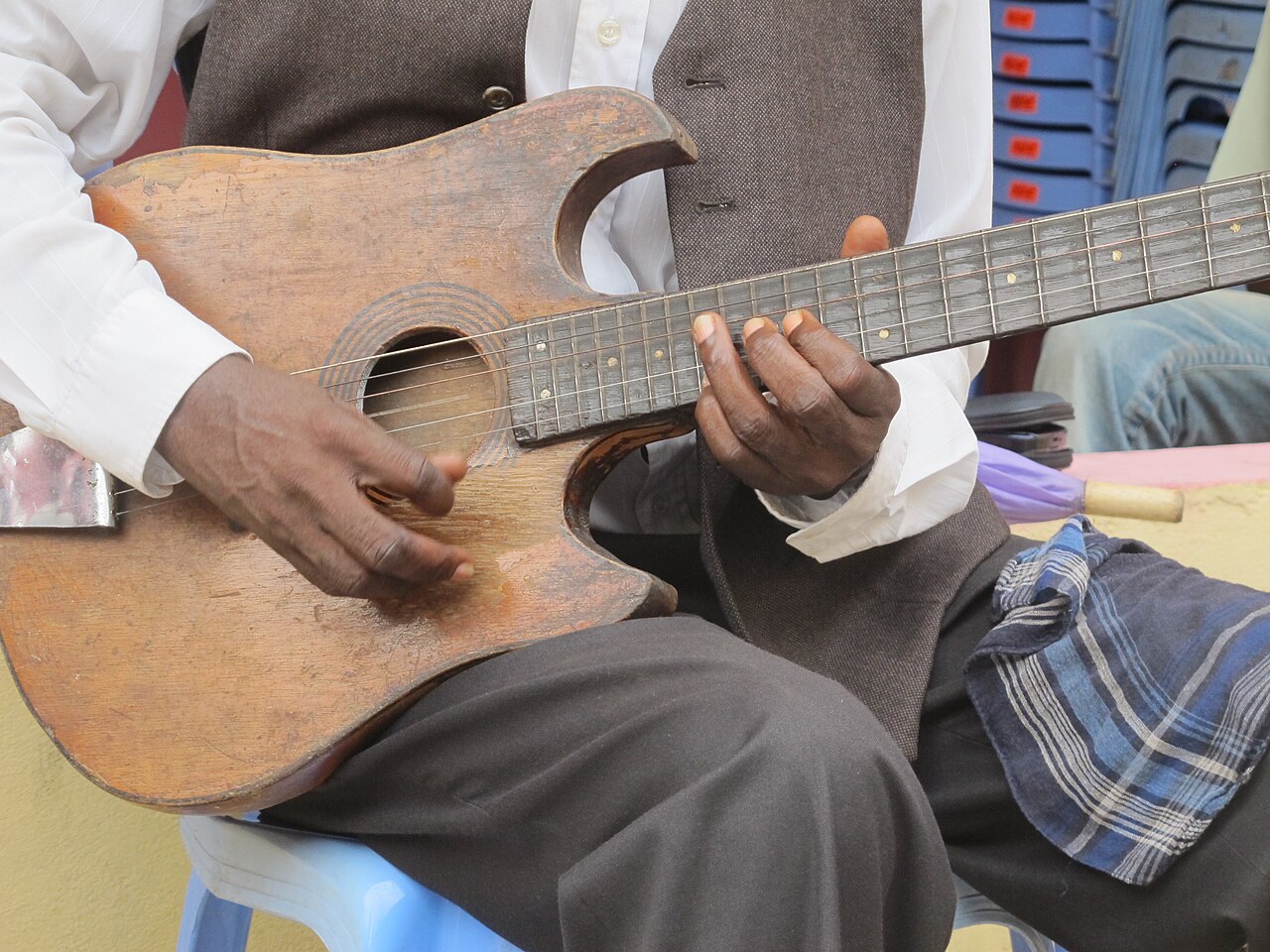 A musician’s hands play a worn wooden guitar.