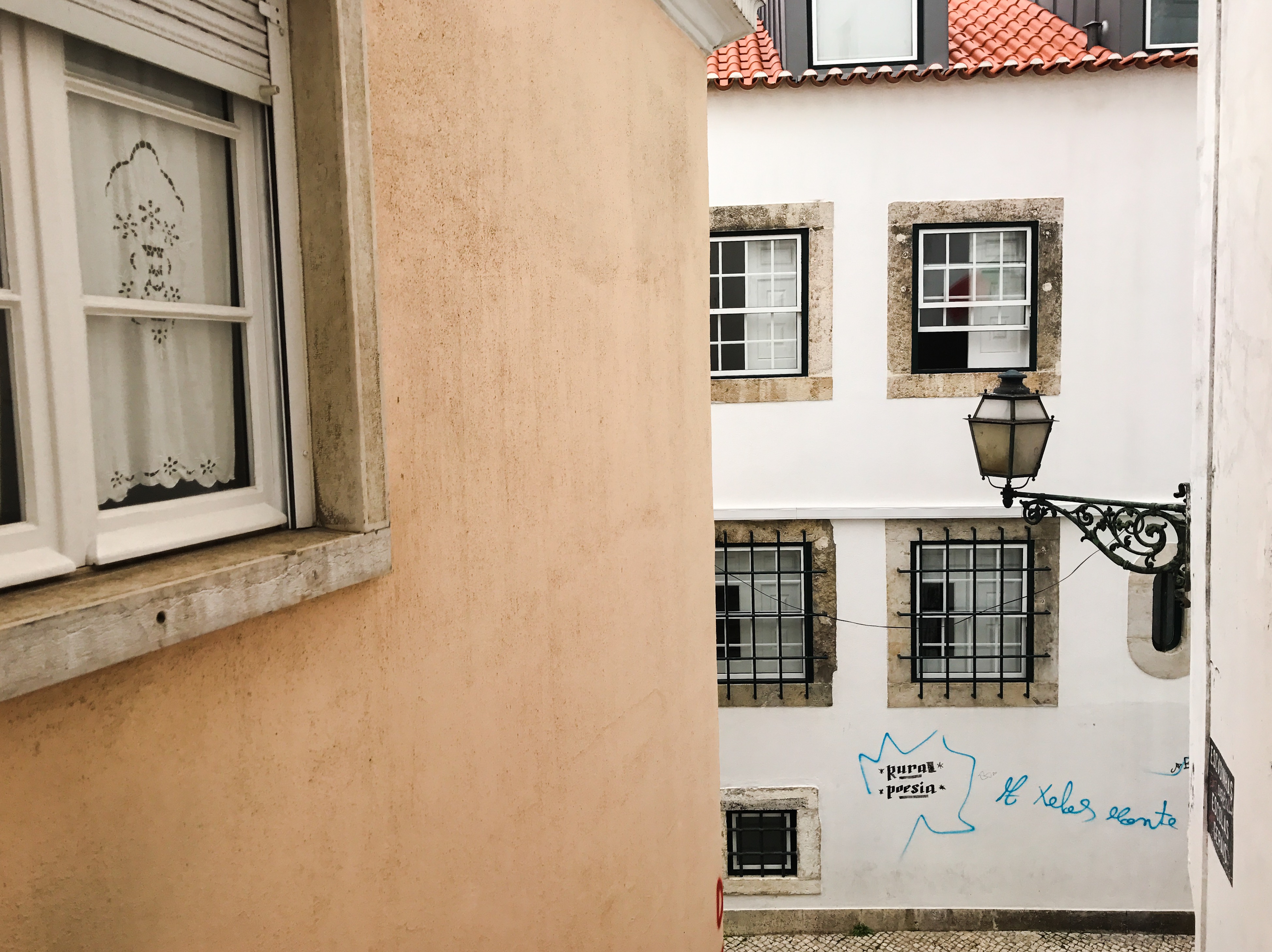 A narrow street lined with pastel buildings and a wall lantern in Alfama, Lisbon