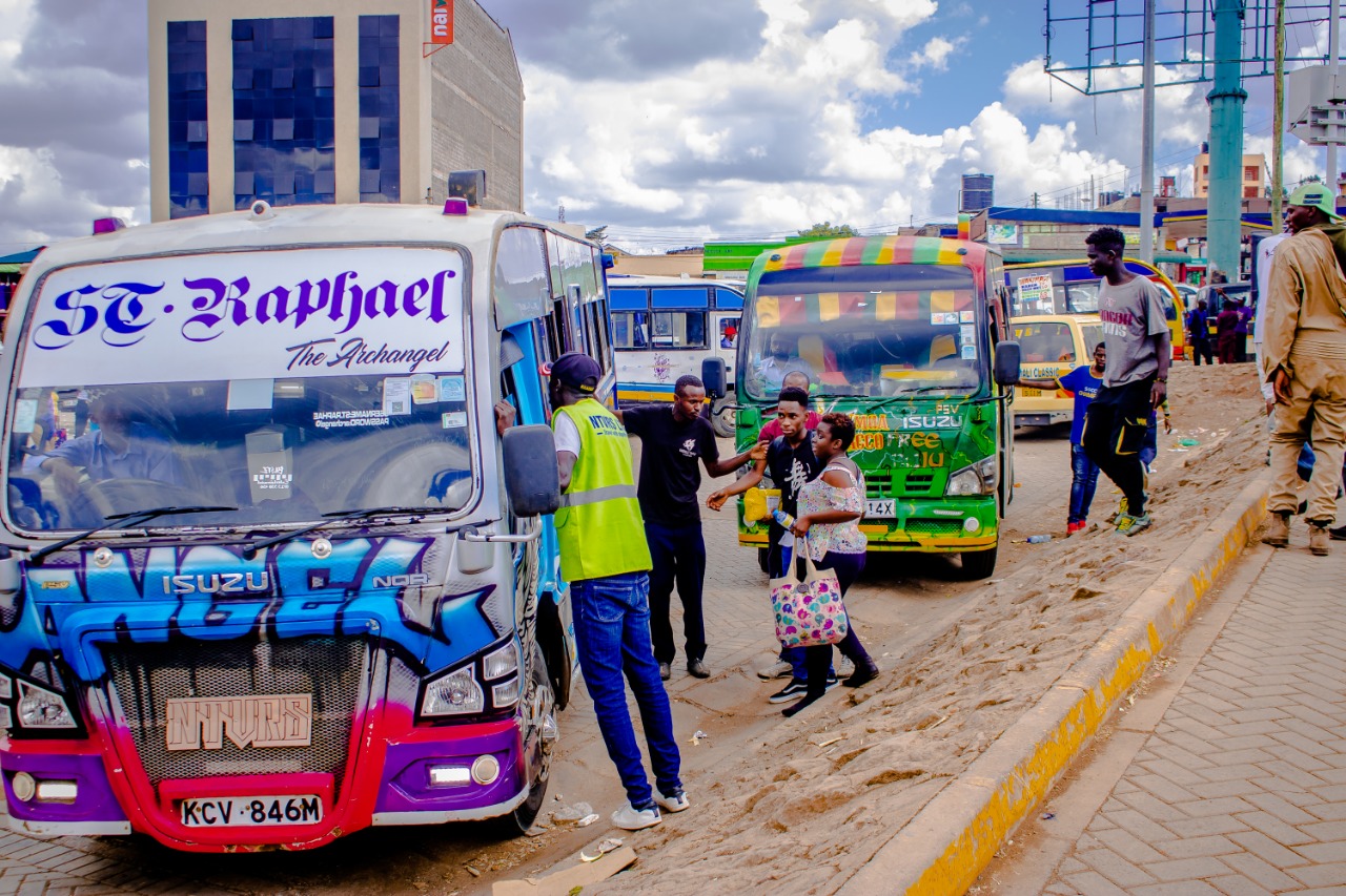 Passengers and crew stand beside brightly painted minibuses.