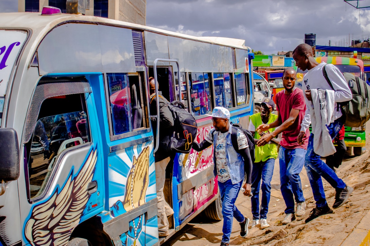 A passenger boarding a decorated minibus while crew members gesture beside the door.