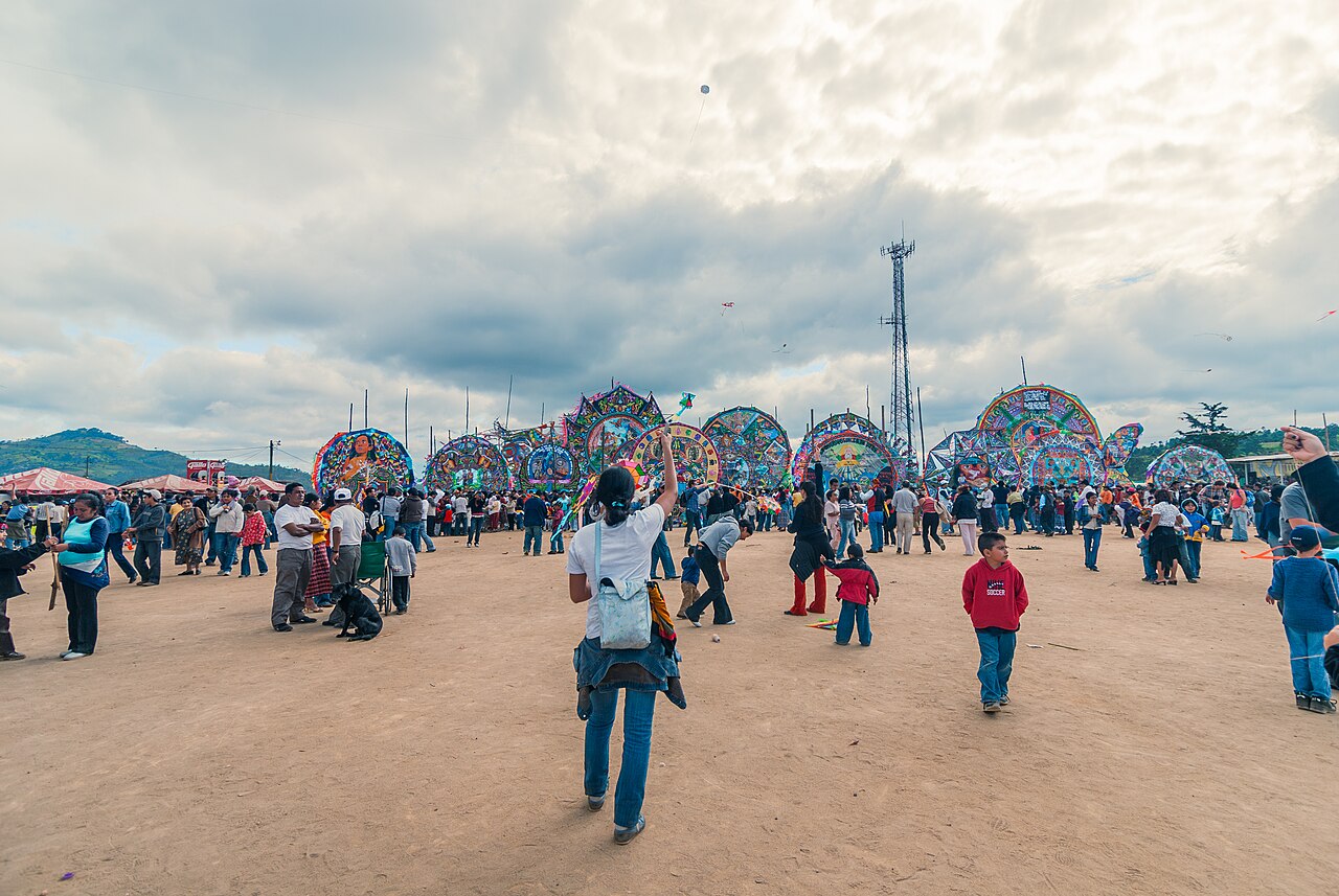 People fly smaller kites across a field, with giant decorated kites behind them.