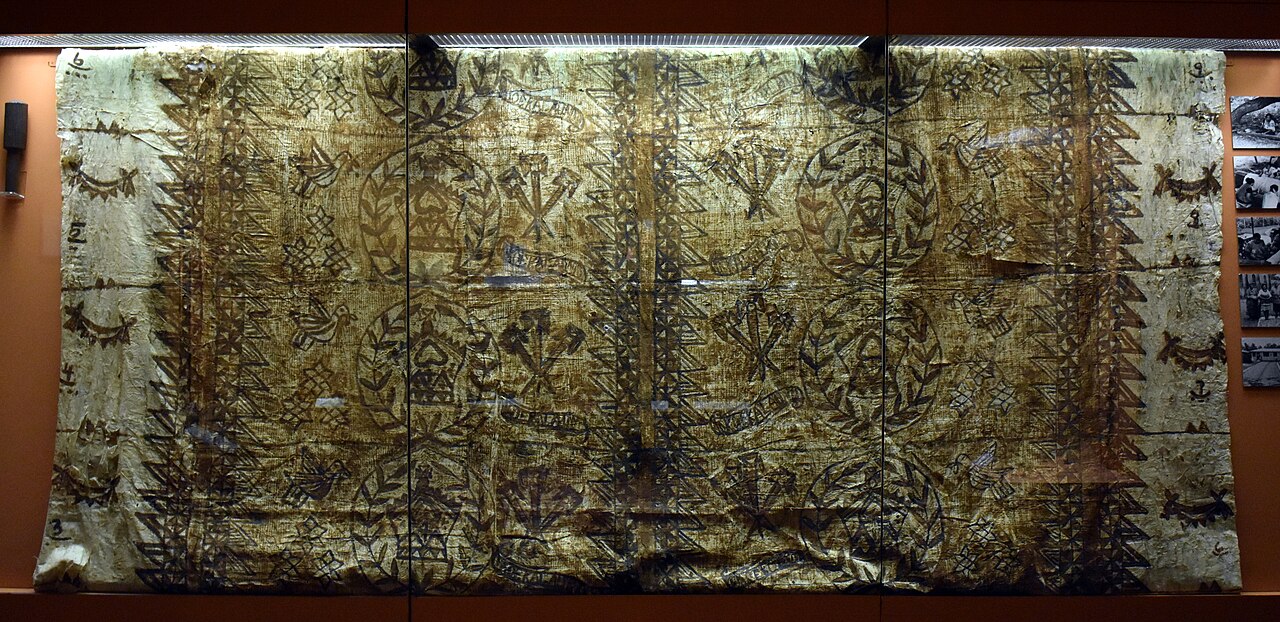 A large patterned cloth behind glass, with numbered borders and repeated plant and bird motifs.
