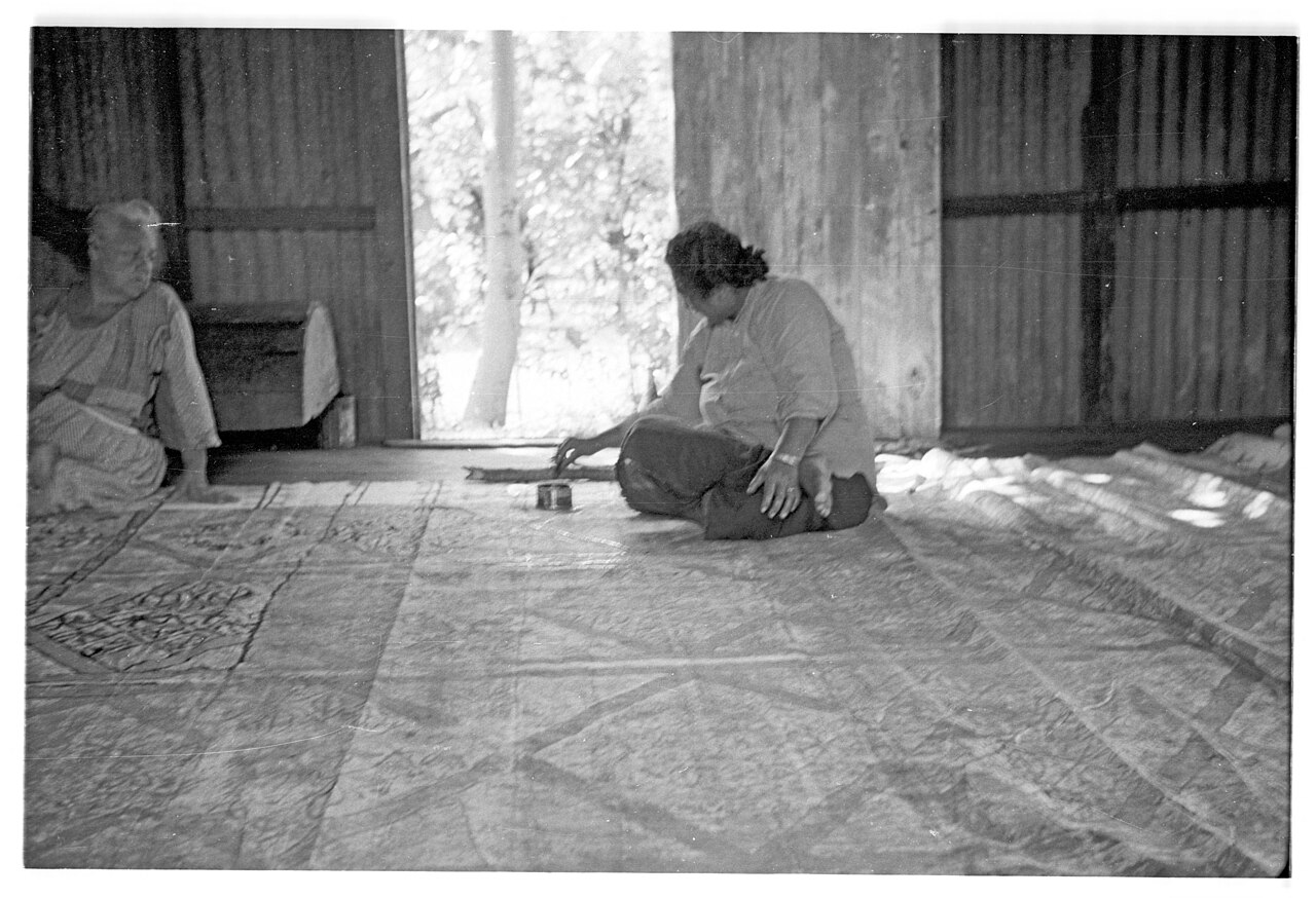 An archival photograph of a woman painting barkcloth.