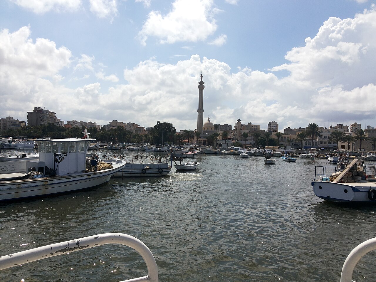 De petites embarcations devant les bâtiments du front de mer et un minaret.