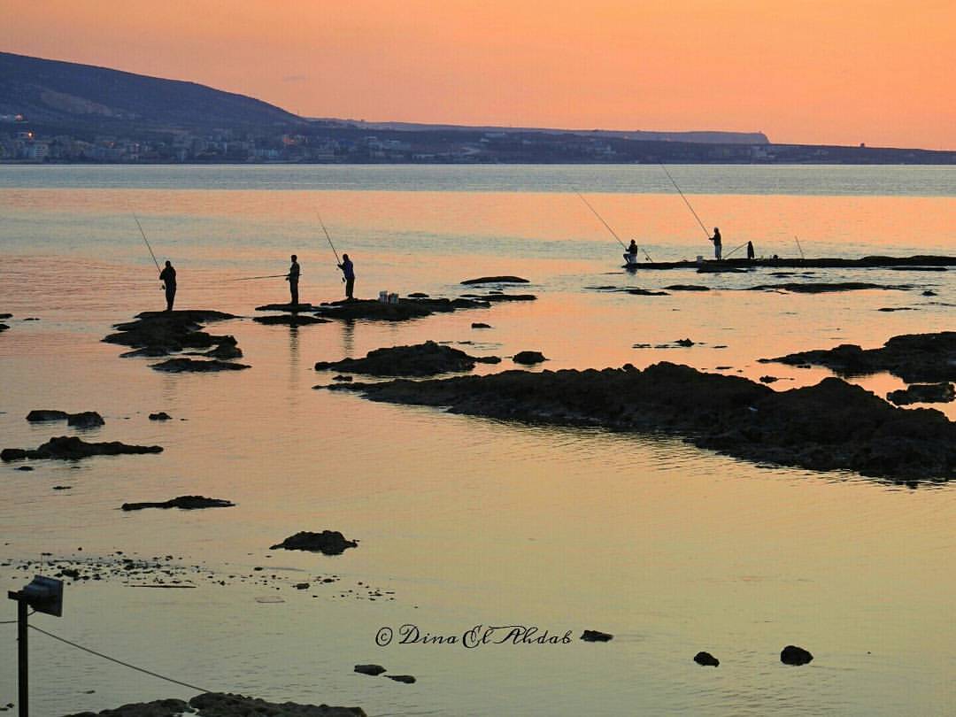 Des personnes au bord de la mer au coucher du soleil.